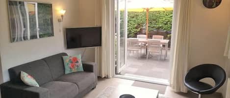 A living room with a sofa, a coffee table, a TV, and a sliding glass door leading to an outdoor area with a table and chairs.