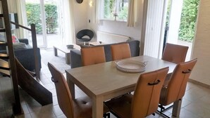 A dining area with a table and chairs, a sofa, a radiator, and a window with curtains. - Holiday Home 3 Minutes from Beach in Domburg - Ooststraat 16 (Domburg)
