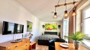 A modern bedroom with a bed, bedside table, TV, and a window with curtains. - Kompakte Ferienwohnung im Seepark Sellin mit Balkon (Sellin)