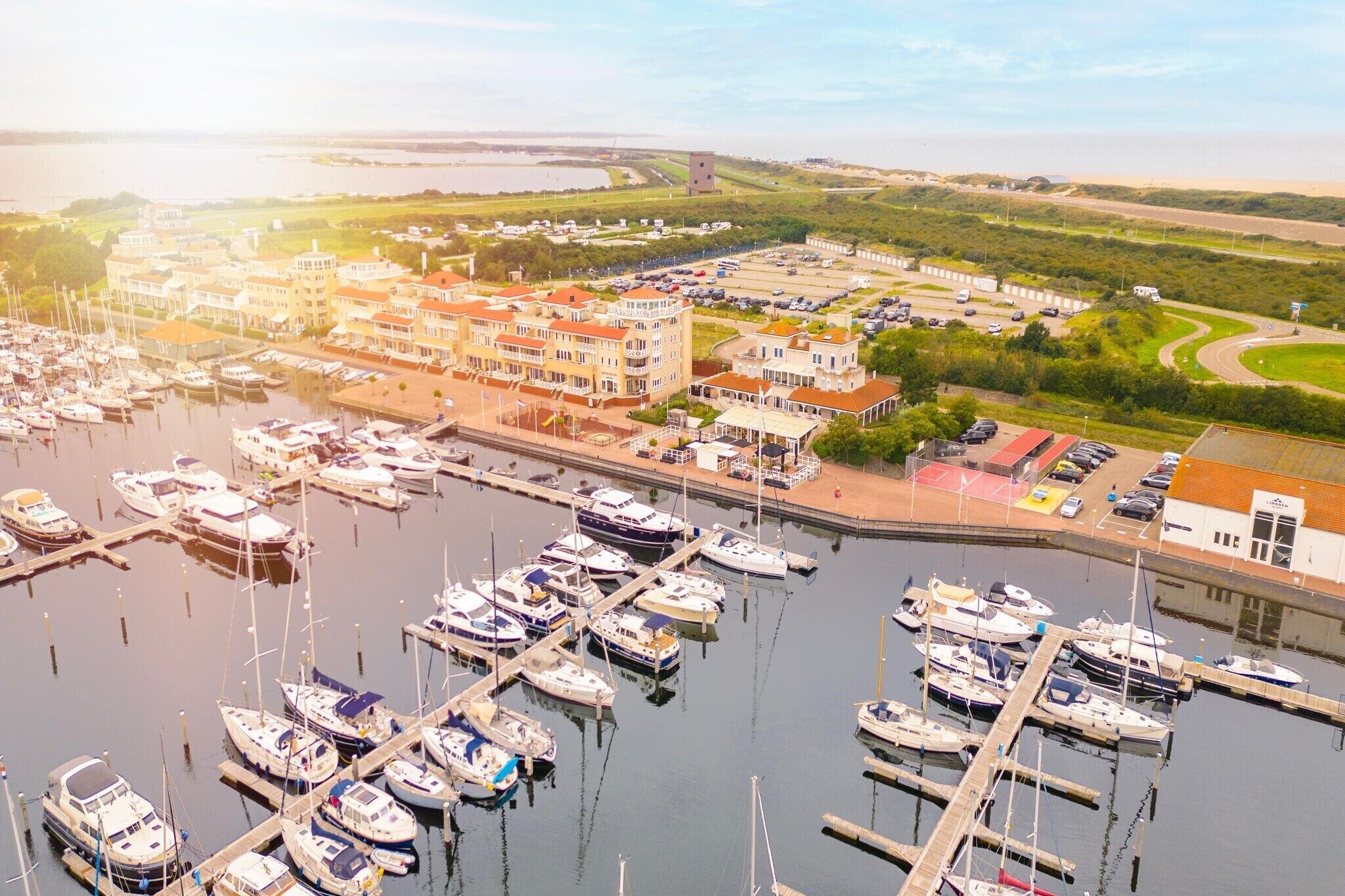 A marina with boats docked, a building with a red roof, and a road curving in the background.