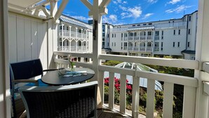 Un espace extérieur abrité, doté d’une table et de chaises, de rampes blanches et offrant une vue sur des bâtiments blancs avec des balcons.