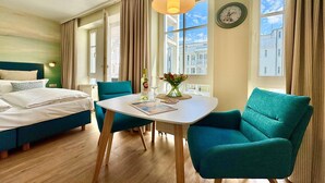 Une chambre d’hôtel avec un lit, une table et des chaises, une fenêtre avec des rideaux et une horloge au mur.