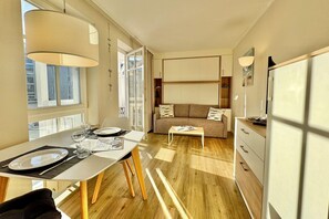 Ein modernes Hotelzimmer mit Essbereich, einer Couch und Blick durch ein großes Fenster.