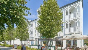A white building with balconies, outdoor seating, and a sign for 'Benedikiner.' - 2 Personen Studio mit Balkon im Seepark Sellin (Sellin)