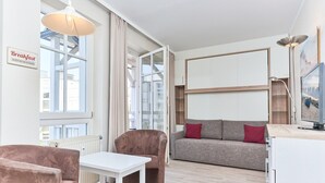A modern living room with a sofa, a chair, a table, and a sign indicating breakfast is served in the kitchen. - 2 Personen Studio mit Balkon im Seepark Sellin (Sellin)
