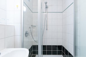 Eine begehbare Dusche mit Glasabtrennung, einer Handbrause, einem Wandarmaturen-Set und einer Glasduschtür.