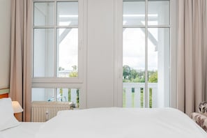 Ein Hotelzimmer mit einem großen Bett, einem Heizkörper, einem Fenster mit Vorhängen und Blick auf Grün.