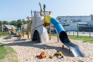 Un parque infantil con un tobogán, estructuras para escalar y arena.