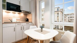 A modern kitchen with white cabinets, a black microwave, and a window with a view of buildings. - Perfekt für Zwei - Fewo mit Balkon und WLAN in Sellin (Sellin)