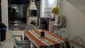 An outdoor dining area with a table and chairs, a brick oven, and a hanging light fixture. - Premium retreat with private pool in Arembepe (Abrantes)