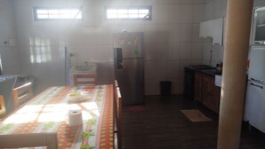 A kitchen with a dining table, chairs, a refrigerator, a sink, and two windows. - Premium retreat with private pool in Arembepe (Abrantes)