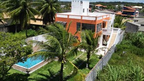 A residential area with a white building featuring a balcony, surrounded by lush greenery and palm trees. - Premium retreat with private pool in Arembepe (Abrantes)