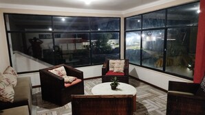 A corner room with large windows, a round table, and two dark wicker chairs. - Premium retreat with private pool in Arembepe (Abrantes)