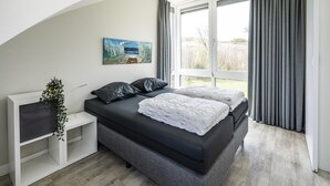 Un dormitorio moderno con cama, un cuadro, una planta y una ventana con cortinas.