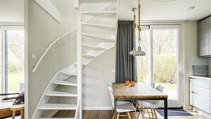 Un interior moderno con una escalera blanca, una zona de comedor con una mesa y sillas de madera, y una cocina.