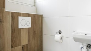 Un baño moderno con inodoro, un dispensador de papel higiénico en la pared y un lavamanos con espejo.