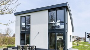 Una casa moderna de dos pisos con amplios ventanales, un patio con mobiliario exterior y un césped bien cuidado.