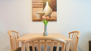 Ett matbord med två stolar, en vas med blommor och en tavla på väggen.