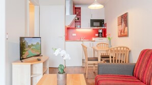 Ett kompakt bostadsutrymme med ett litet kök, en matplats, en soffa och en tv.