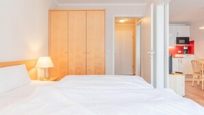 Ett hotellrum med en säng, ett nattduksbord, en lampa, en garderob i trä och ett litet kök med mikrovågsugn och kaffebryggare.