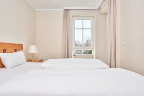 Ein Hotelzimmer mit einem großen Bett, einem Nachttisch mit Lampe und einem Fenster mit Vorhängen.