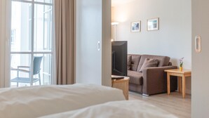 Ein Hotelzimmer mit Bett, Sofa, Fernseher, einem kleinen Tisch mit Pflanze und einem Fenster mit Vorhängen.