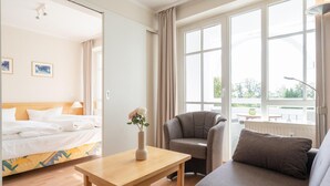 Una habitación de hotel con cama, sofá, sillón, mesa y ventanas amplias.