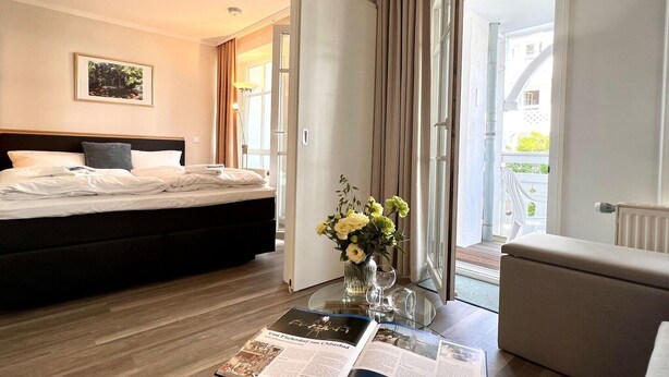 Ett hotellrum med en säng, ett glasbord med ett tidningsnummer, en vas med blommor och utsikt över omgivningen.