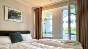 Ett hotellrum med en säng, ett fönster, en lampa och en inramad tavla på väggen.