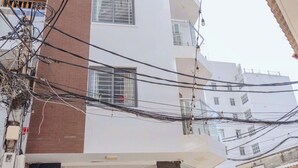 Un edificio de varios pisos con fachada blanca y detalles en marrón, que cuenta con una entrada a nivel de calle con una planta en maceta y una motocicleta estacionada afuera.
