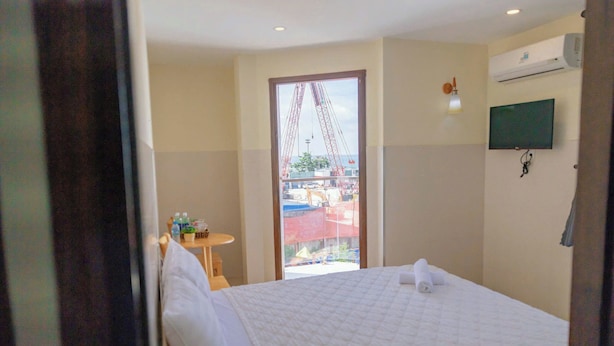 Habitación de hotel con cama, televisión montada en la pared, ventana con vista a una obra en construcción y una mesita con agua embotellada.