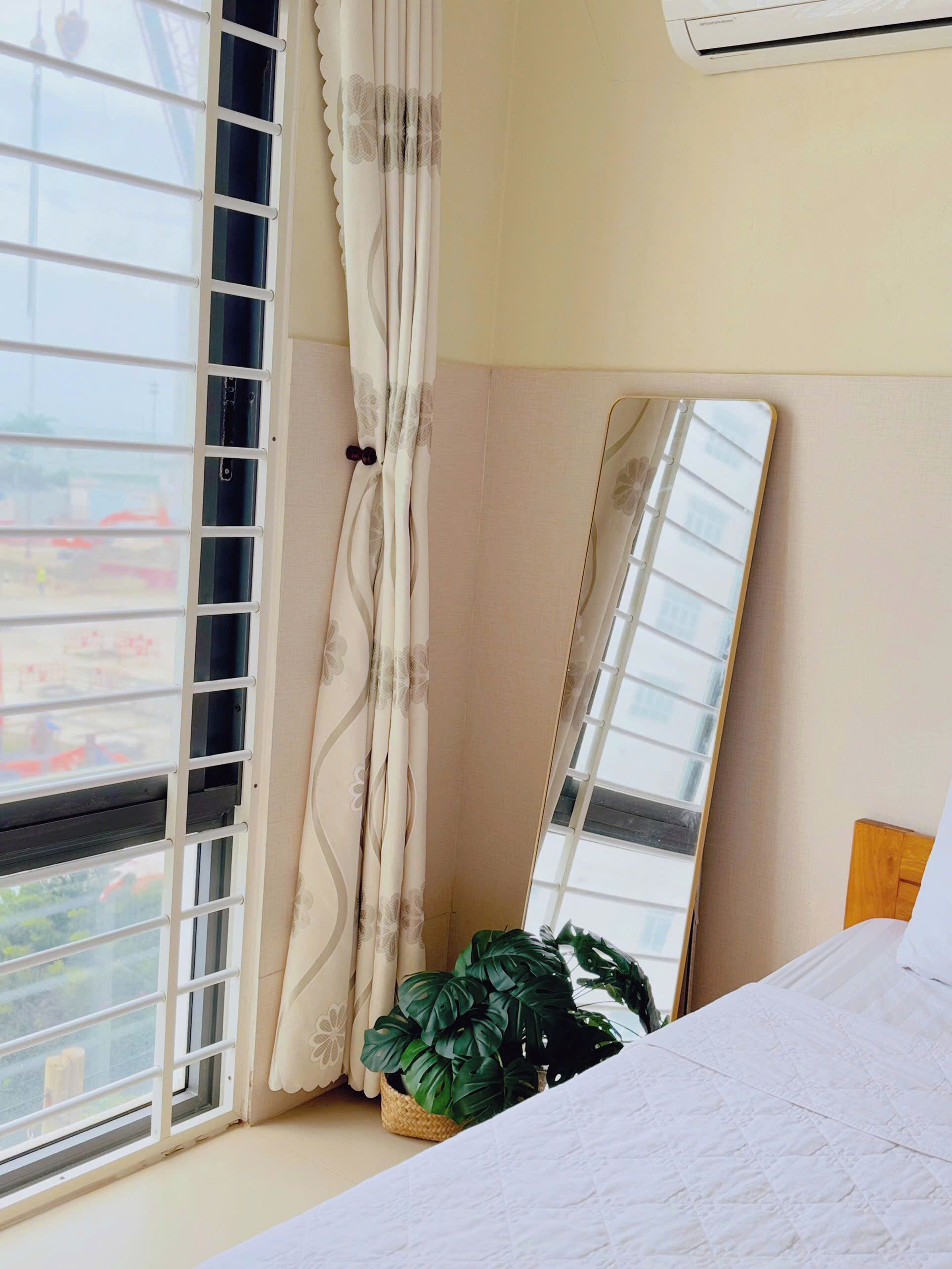 Une chambre avec une grande fenêtre, un miroir, un lit et une plante en pot.