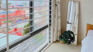 Una habitación con un ventanal grande, una planta en maceta, una cama y un equipo de aire acondicionado.