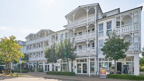 A multi-story building with balconies, a paved entrance area, and a storefront with a sale sign. - Stilvolle Ferienwohnung mit Balkon in Sellin (Sellin)