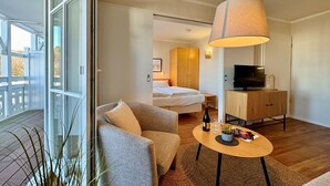 A hotel room with a bed, a sofa, a TV stand, and a dining table. - Stilvolle Ferienwohnung mit Balkon in Sellin (Sellin)