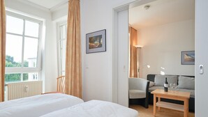 A hotel room with two beds, a sofa, a small table with a bottle and glasses, and a picture on the wall. - Ferienwohnung in Sellin mit Balkon und WLAN (Sellin)