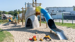 En legeplads med rutchebane, klatrestrukturer og sand.