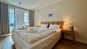 A hotel room with a large bed, two bedside tables, a window with curtains, and a view of the outside. - Stilvoll eingerichtete Ferienwohnung mit großem Balkon in Sellin (Sellin)