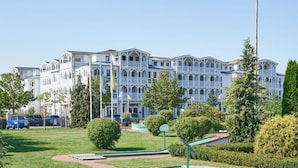 Ein großes, mehrgeschossiges Gebäude mit einer symmetrischen Fassade, mehreren Balkonen und einem gepflegten Rasen mit einer kleinen Spielanlage.