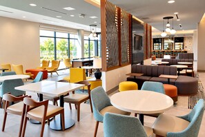 A modern interior with round tables and chairs, a seating area with sofas, and a large window providing a view of the outdoors. - Hawthorn Extended Stay by Wyndham Central McKinney (McKinney)