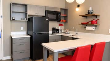 Cocina pequeña equipada con refrigerador, microondas, cafetera y un lavamanos.