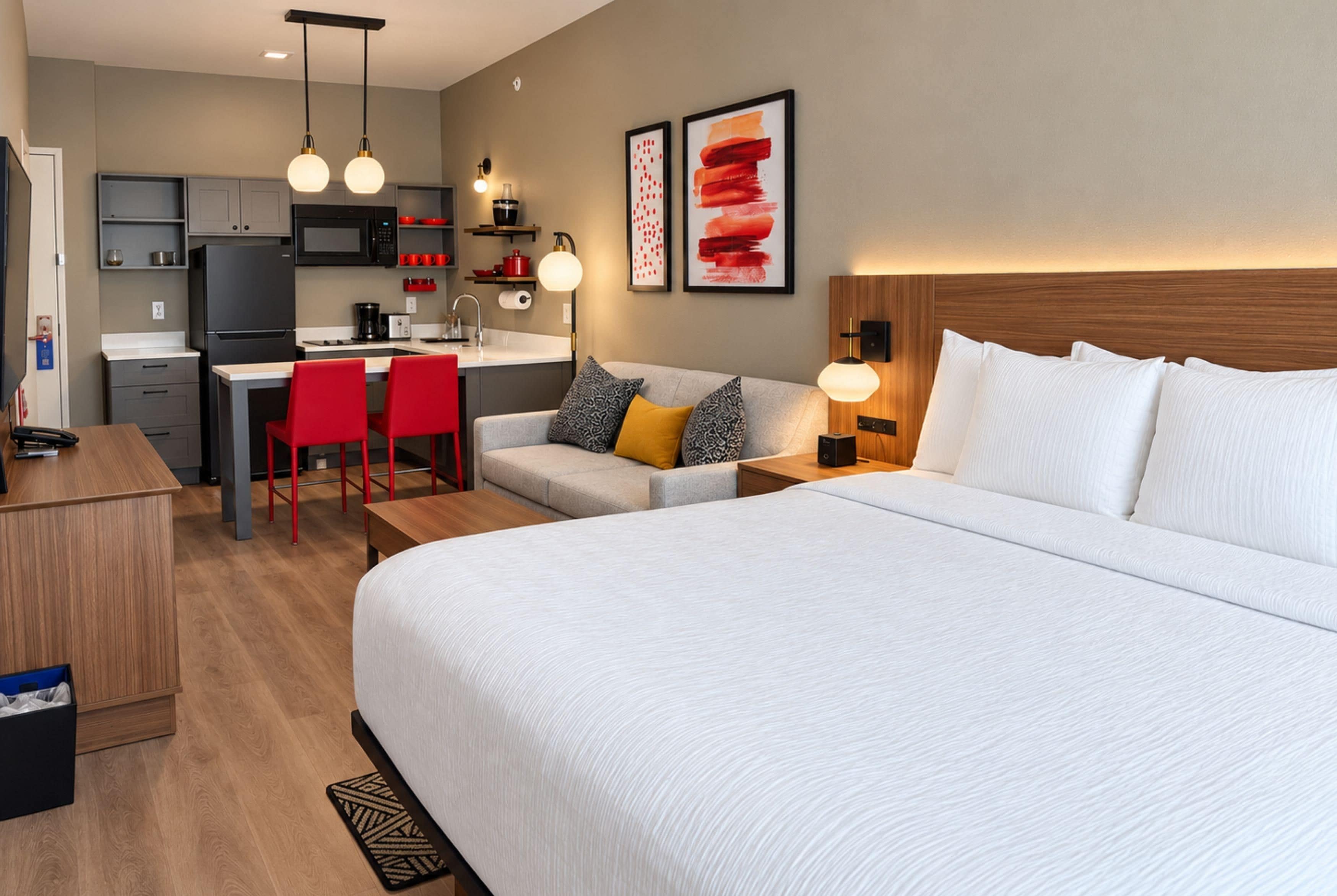 Habitación de hotel con una cama grande, un sofá, un escritorio con sillas, una zona de cocina y obras de arte en las paredes.