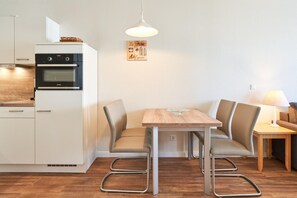 Een compacte keuken met een inbouwoven, een eethoek met een tafel en stoelen, en een wandlamp.