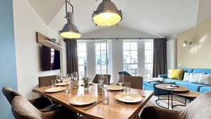 Un coin repas avec une table en bois dressée pour quatre personnes, deux lampes suspendues et un canapé bleu en arrière-plan.