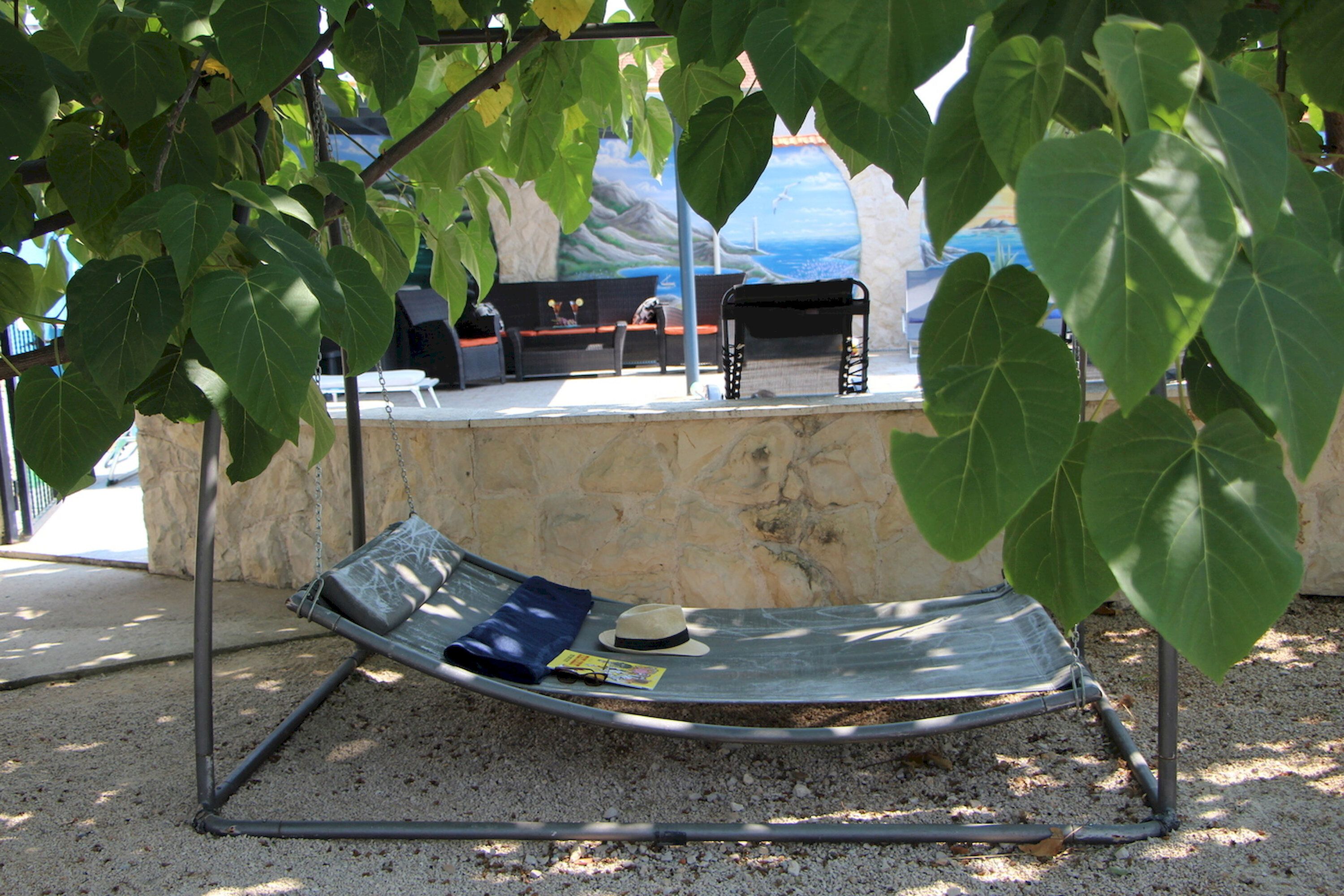A hammock under a tree, a stone wall, and a bench with a hat and magazine.