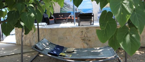 A hammock under a tree, a stone wall, and a bench with a hat and magazine.