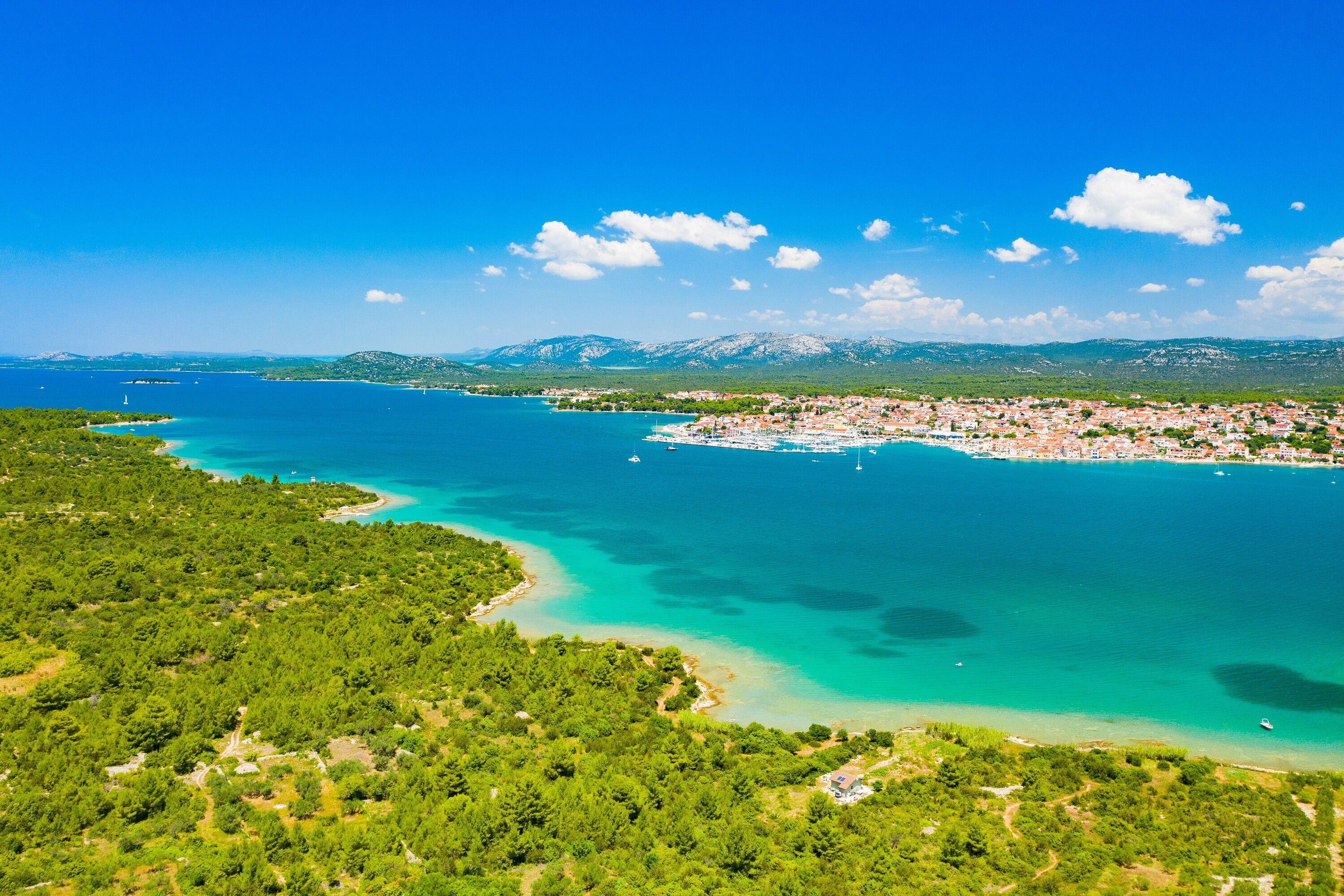 A coastal town with a marina, surrounded by mountains and clear blue waters.