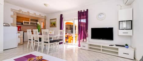 A modern living room with a dining area, a kitchen, and a TV.