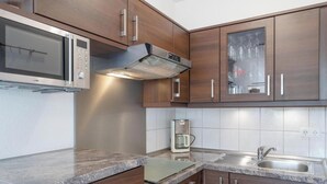A kitchen with wooden cabinets, a stainless steel microwave, a coffee maker, and a sink. - Ferienwohnung mit Balkon und Fitnessbereich in Sellin (Sellin)