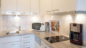 Een moderne keuken met witte kastjes, een ingebouwde magnetron, een koffieapparaat en een spoelbak.